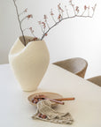 Elegant dining vignette featuring a sculptural ceramic vase with berry branches and KULALA handcrafted wooden salad servers in a shallow stoneware bowl and linen face washer