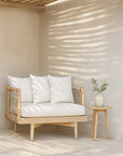 One Seater Tamala Sofa with teak frame and white cushions styled in a sunlit outdoor lounge with natural textures and a round side table