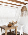 Natural warm brown teak carved bowl styled on a rustic timber outdoor dining table with white wicker chair, woven pendant and soft coastal light.