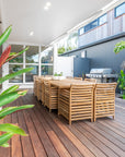 A spacious outdoor dining setting featuring a solid teak table and matching slatted dining chairs, designed for elegant alfresco entertaining on a timber deck