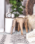 A cosy fireplace nook featuring a natural teak root side table, a woven egg chair with plush cushions, a chunky knit throw, and layered textures for a warm, inviting atmosphere