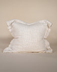 A textured linen cushion in a ivory tone, featuring a relaxed, oversized design with raw-edge detailing, set against a neutral backdrop