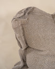 A textured linen cushion in a natural beige tone, featuring a relaxed, oversized design with raw-edge detailing, set against a neutral backdrop