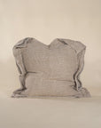 A textured linen cushion in a natural beige tone, featuring a relaxed, oversized design with raw-edge detailing, set against a neutral backdrop