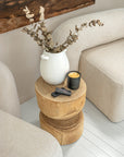 Close-up of a timber side table styled with a white ceramic vase, dried eucalyptus, KULALA Living black candle, and matches nestled between two boucle nash armchairs.