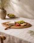 Vara cheese board in teak styled with cheese, grapes and crackers on a soft neutral table setting.