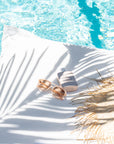 White bean bag pillow by the poolside with sunglasses, straw hat, and sunscreen, creating a serene summer relaxation scene.