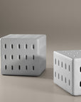 A modern white concrete table with perforated details, blending sculptural design with functional seating for indoor and outdoor spaces