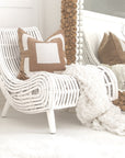 A stylish white rattan lounge chair with an organic, sculptural form, featuring a handwoven frame and elegant wooden legs. Styled with neutral cushions and a cosy throw, creating a relaxed and inviting living space