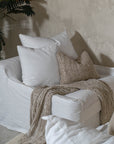 White linen one seater sofa styled with neutral textured cushions and a knitted throw in a minimalist living room setting