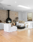 Bright and airy living room styled with white linen sofas, natural timber flooring, a black fireplace and soft neutral décor by KULALA Living.