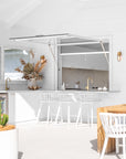 Bright white outdoor bar with white teak barstools, a brass tap, natural timber accents, and dried floral arrangement for a breezy, coastal entertaining space.