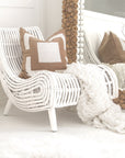 A stylish white rattan lounge chair with an organic, sculptural form, featuring a handwoven frame and elegant wooden legs. Styled with neutral cushions and a cosy throw, creating a relaxed and inviting living space
