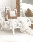 A stylish white rattan lounge chair with an organic, sculptural form, featuring a handwoven frame and elegant wooden legs. Styled with neutral cushions and a cosy throw, creating a relaxed and inviting living space