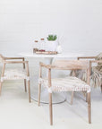 White round dining table with natural timber chairs featuring white woven seats, creating a contemporary and relaxed dining setting.