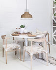 White round dining table with natural timber chairs featuring white woven seats, creating a contemporary and relaxed dining setting