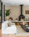Relaxed living space featuring a white linen slipcover sofa, textured neutral cushions, black wood fireplace, earthy ceramic vases, and layered natural textures by KULALA Living.