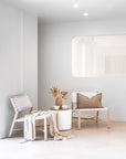 A serene lounge setting featuring natural wood lounge chairs with woven white leather seats and backrests, styled with neutral textiles and earthy décor