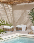 Zahara Ottoman featuring handwoven rattan weave with white cushion, styled poolside under slatted timber shade with palm plants and soft natural light