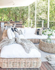 Natural wicker ottoman with a plush white cushion, creating a relaxed vibe on a deck surrounded by trees.