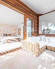 Coastal-inspired bedroom with natural wicker corner sofa featuring white cushions, complemented by a wooden bench and pendant lighting
