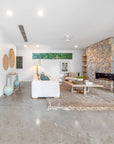 Modern lounge room with a natural aesthetic, featuring a neutral modular sofa with green cushions, a wooden coffee table with decor accents, woven wall hangings, and a textured floor rug