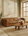 Zanele Three Seater Sofa in tan leather styled with a neutral throw in a modern living room featuring a timber coffee table, cactus planter, and soft natural light