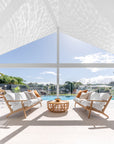 Kulala Living outdoor setting featuring teak sofas with plush white cushions and a rattan coffee table, overlooking a serene poolside view. Perfect for relaxed, resort-style living