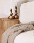A beautifully styled living space featuring KULALA Living’s brass candlestick holders on a sculptural wooden side table. The warm, neutral tones of the boucle swivel chair, soft throw, and textured rug create an inviting and sophisticated setting with organic elegance