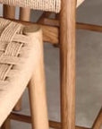 Close-up of KULALA Living teak barstools with woven seats, styled in a light-filled kitchen with white island bench, brass tapware, and artisanal tile splashback.