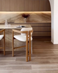 Pair of light oribberwood and boucle counter stools at a marble island bench in a contemporary kitchen with timber cabinetry and natural stone splashback.
