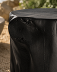 Black magnesium oxide stools arranged around an outdoor fire pit in a coastal garden retreat, creating a relaxed gathering space framed by native greenery and ocean views.