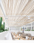Bright and airy outdoor seating area under a white bamboo pergola, featuring natural timber tables, beige lounge seating, and a cactus planter for a relaxed, resort-style atmosphere