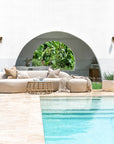 Beige outdoor sofa with cushions by a pool, featuring a circular mirror reflecting greenery.
