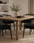 Dining room with wooden table and black chairs, featuring a vase with greenery.