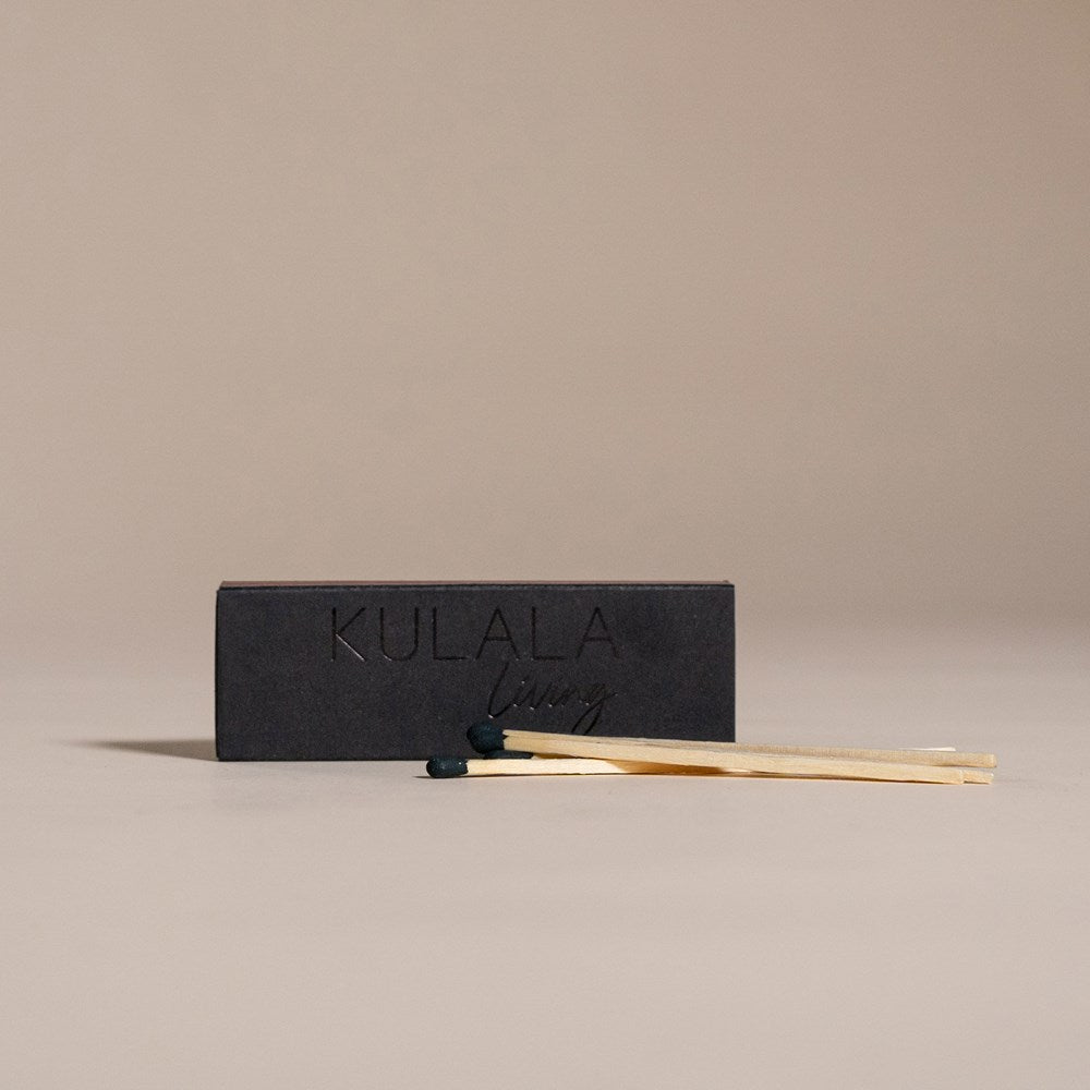 Kulala Living black matchbox with minimalist branding, featuring long wooden matches with black tips, set against a neutral backdrop for a refined aesthetic