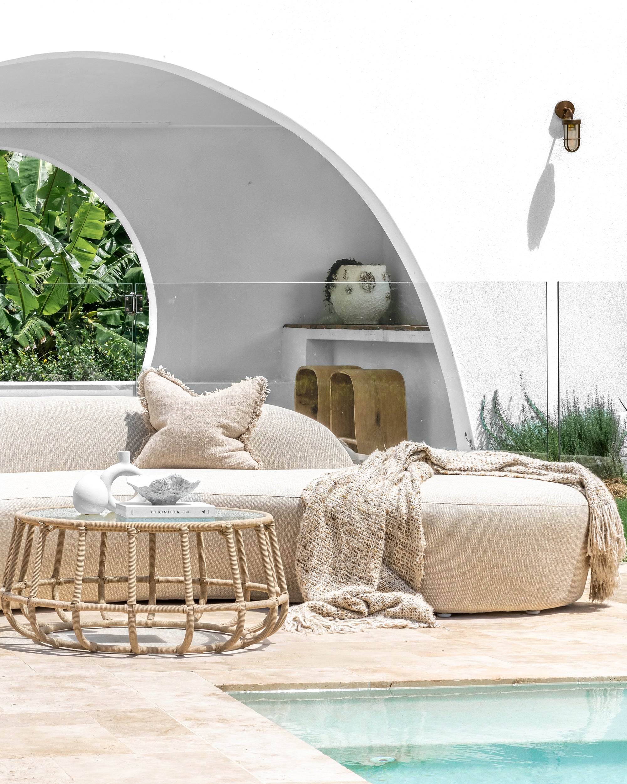 Outdoor seating area with a sofa, coffee table, and decorative items by a pool.