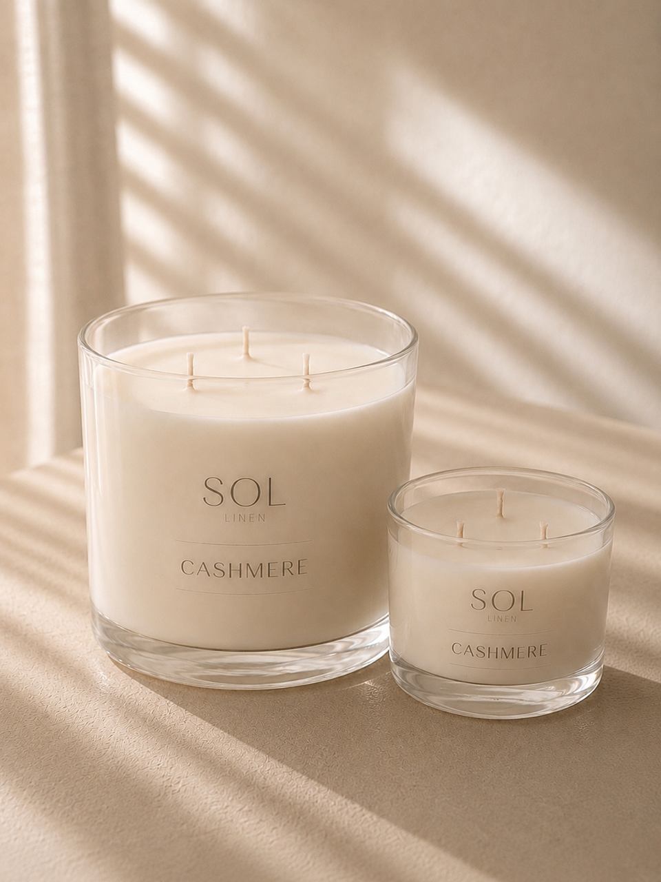 Two SOL Candle Co. Cashmere scented candles in clear glass jars, one large and one small, styled on a beige surface with soft window shadow patterns.