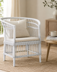White wicker chair with beige cushion in a room with a wooden side table and books.