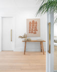 Wooden console table with decorative items against a white wall, featuring a framed abstract art piece.
