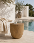 Wooden side table by a pool with a blanket and vase in the background