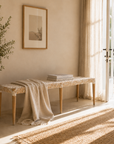 Woven bench with a blanket in a sunlit room with a plant and framed picture.
