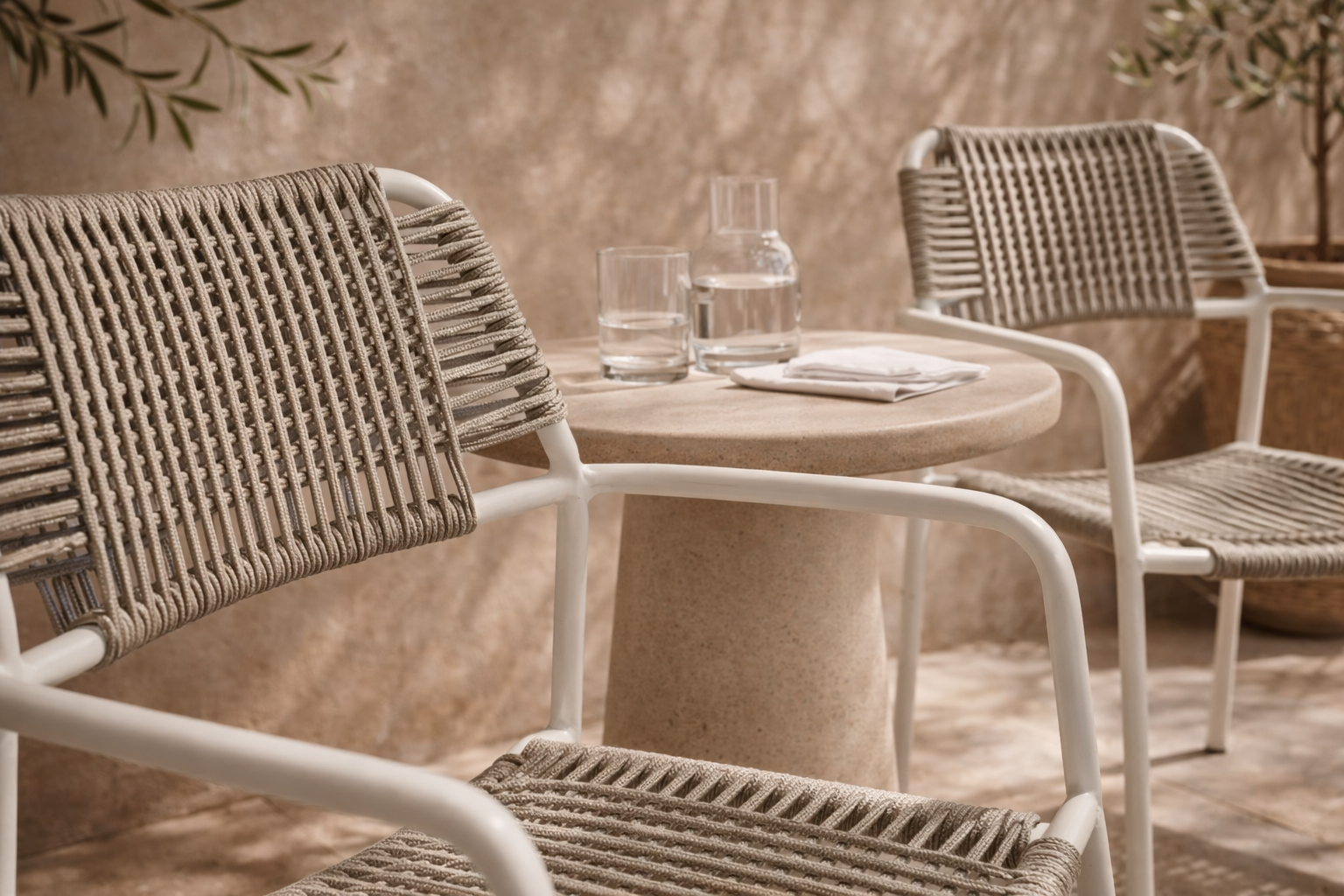 Amila armchair in white with natural rope weave styled in a sunlit mediterranean courtyard with textured walls and stone table