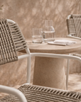 Amila armchair in white with natural rope weave styled in a sunlit mediterranean courtyard with textured walls and stone table