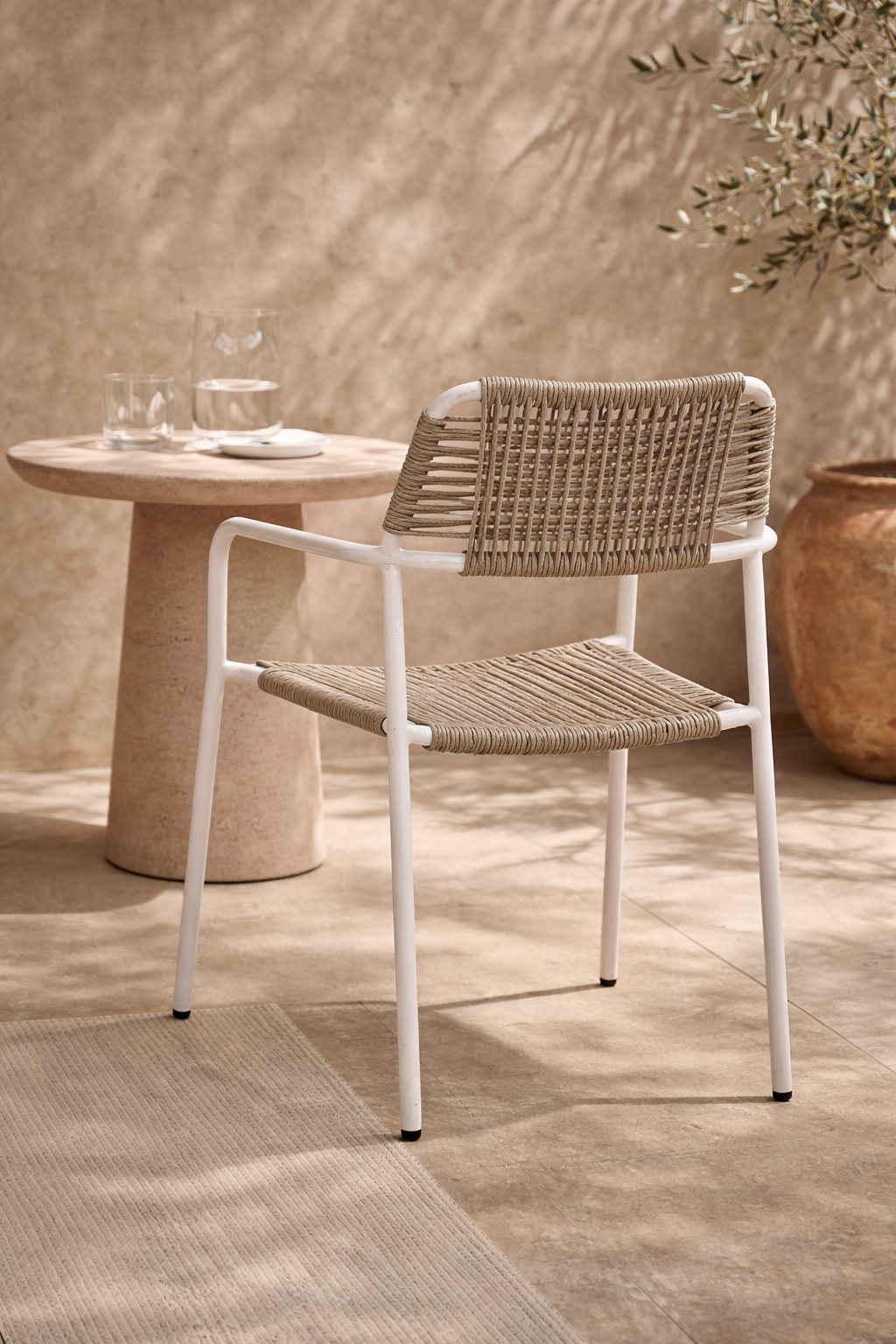Amila armchair in white with natural rope weave styled in a sunlit mediterranean courtyard with textured walls and stone table