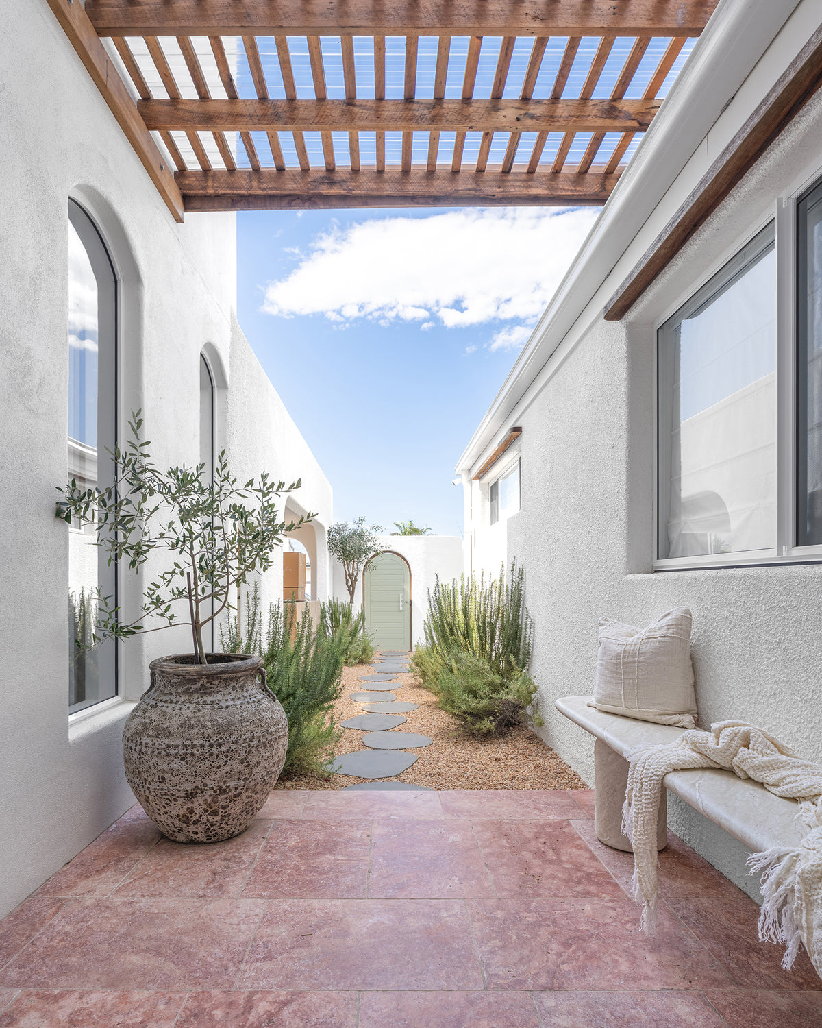 KULALA Living Ayanda Concrete Bench in Eggshell styled with the Fara Linen Bath Towel and Meadow Linen Square Cushion in a sunlit coastal courtyard with natural stone paving, a timber pergola and Mediterranean inspired greenery.
