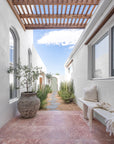 KULALA Living Ayanda Concrete Bench in Eggshell styled with the Fara Linen Bath Towel and Meadow Linen Square Cushion in a sunlit coastal courtyard with natural stone paving, a timber pergola and Mediterranean inspired greenery.