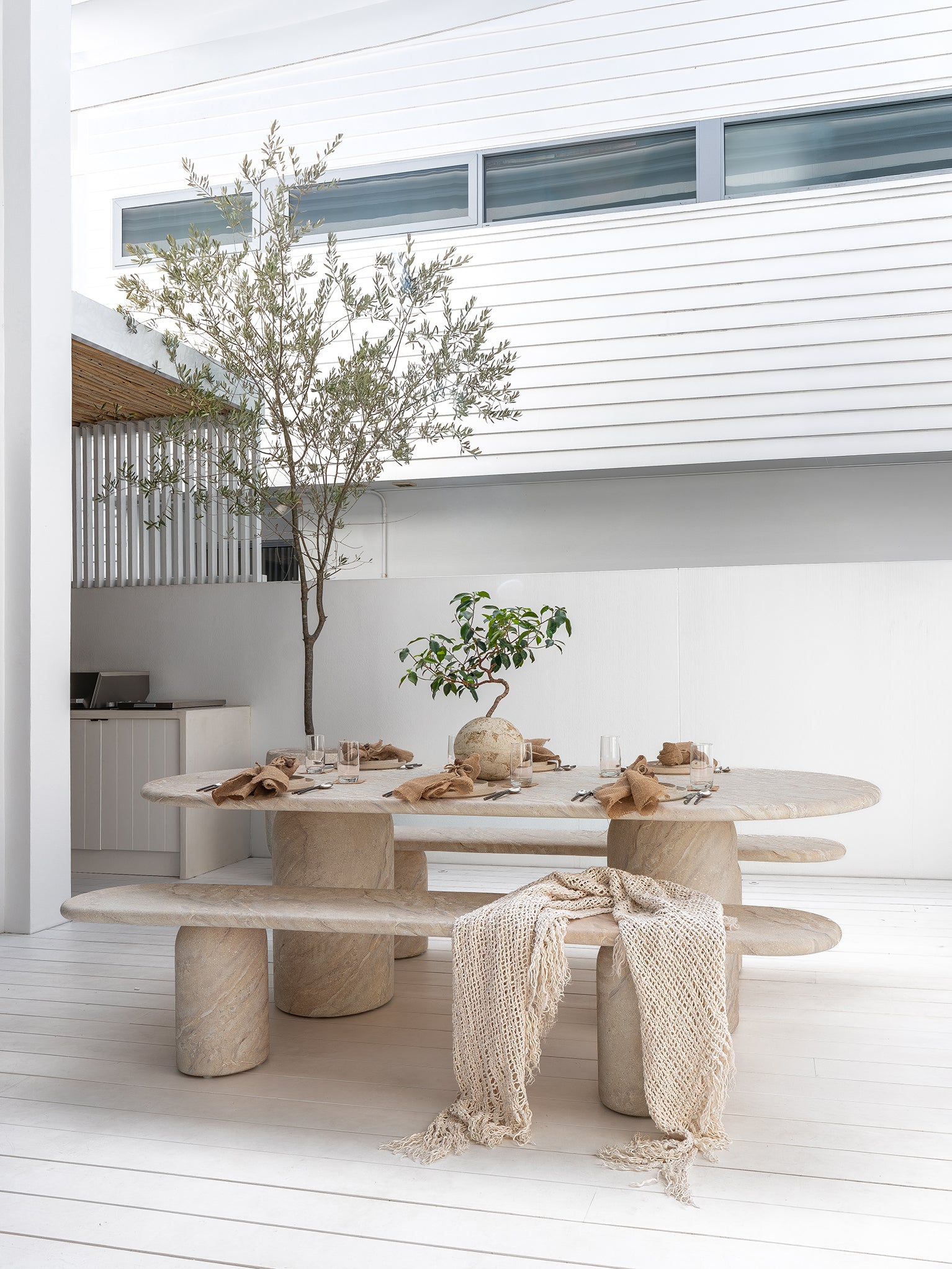 Ayanda dining table and bench in dune finish styled in a light filled outdoor space with natural textures and relaxed coastal dining atmosphere.