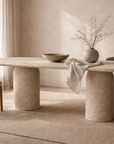 Ayanda dining table in dune hydro dipped finish with oval top and cylindrical pedestal bases styled in a warm neutral dining space.