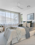 Serene bedroom featuring soft linen bedding in neutral tones, plush cushions, and a cosy throw, complemented by the Makena Chair in the corner, styled with a decorative cushion and blanket
